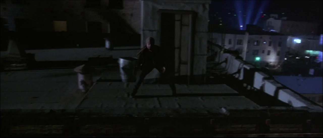 Strange Days (1995) movie still: wide — A flat-topped urban building roof at night under dark, low-visibility conditions. A man in dark clothing…