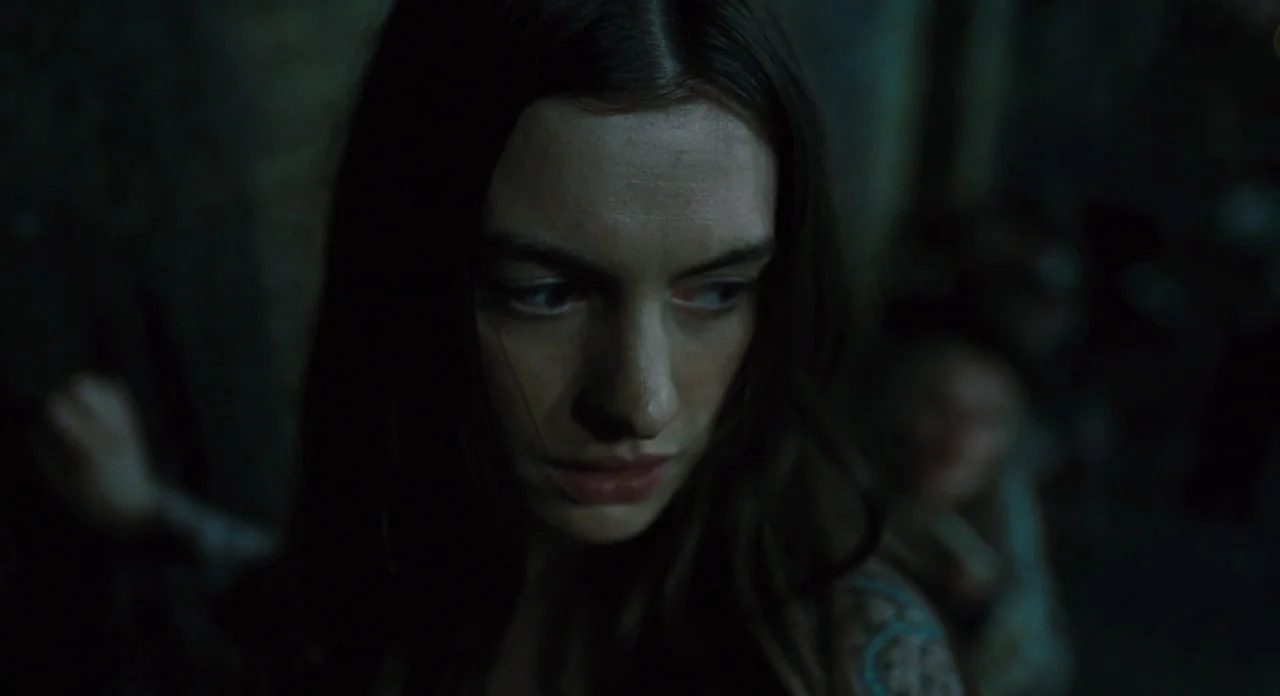 Les Misérables (2012) movie still: closeup — A dark, dimly lit stone interior space with muted colors. A woman with long brown hair looks toward the…