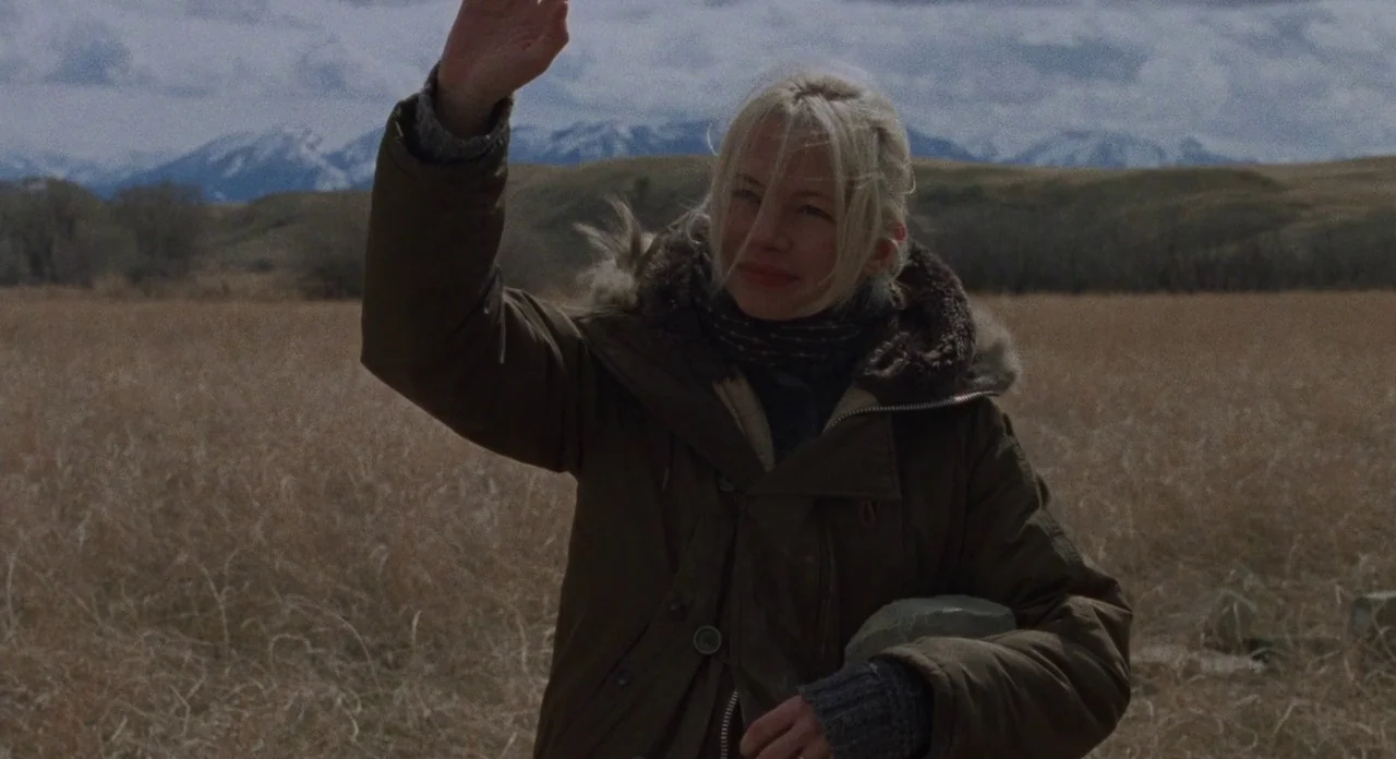 Certain Women (2016) movie still: medium — A woman stands in a vast, dry, brownish-tan field beneath an overcast sky. Behind her are distant,…