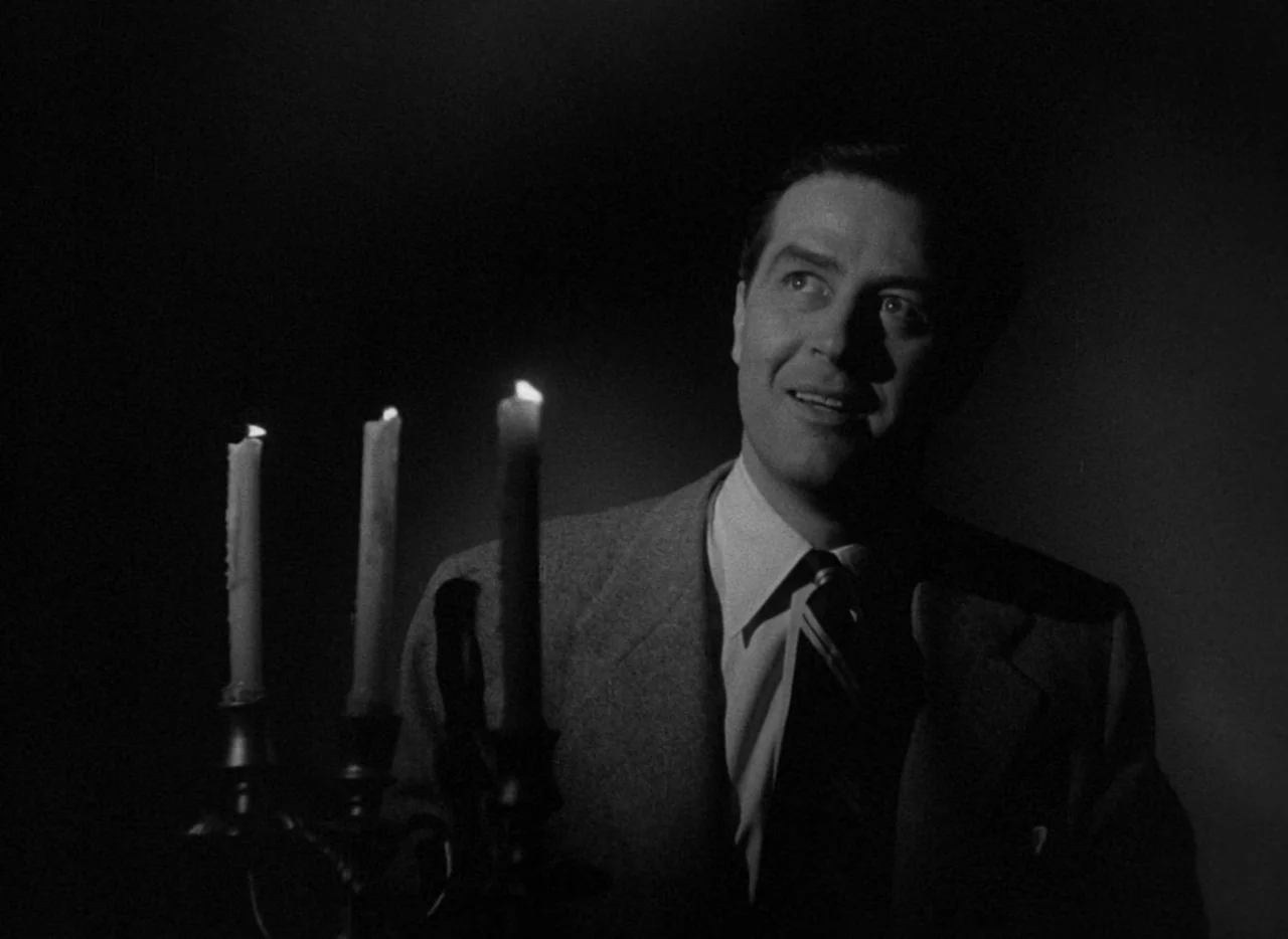 The Uninvited (1944) movie still: medium — A man stands in a dark environment illuminated only by a small candle flame. He holds a candelabra and…