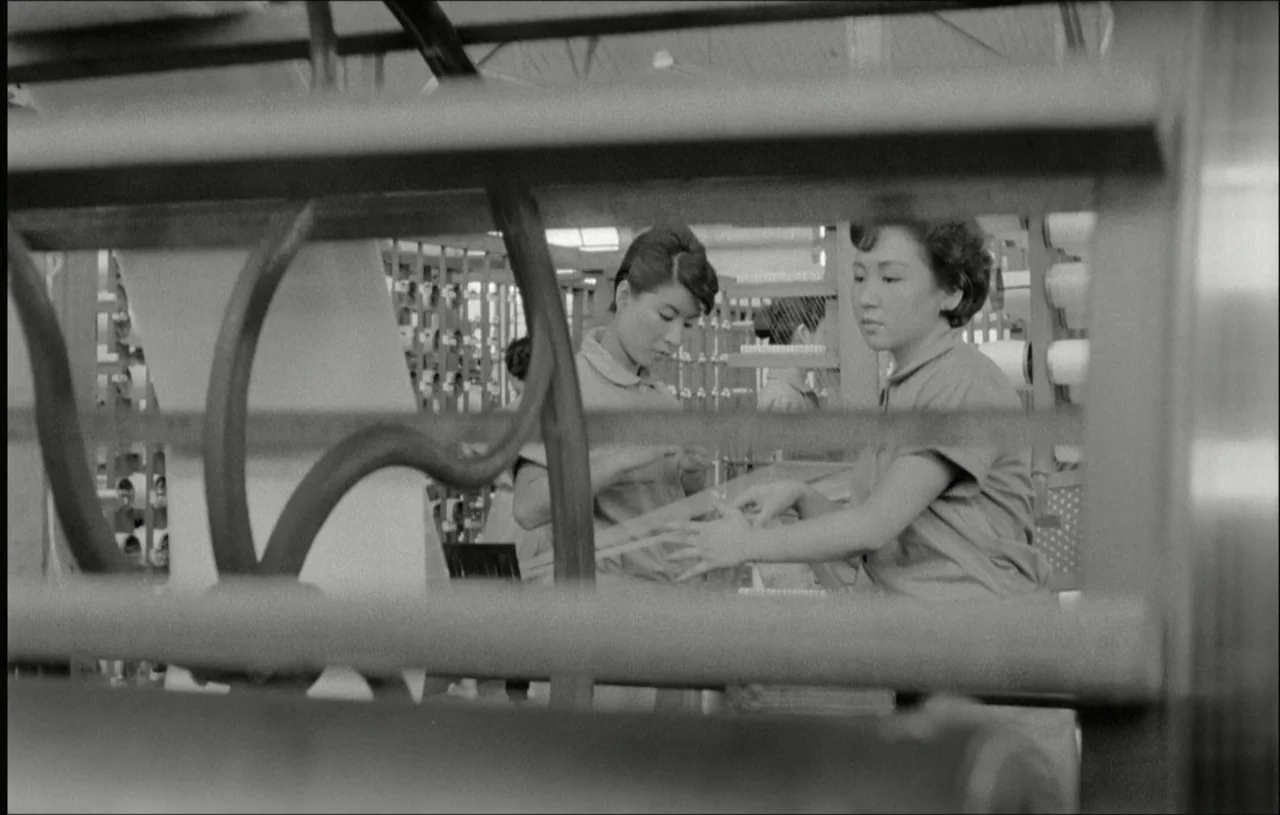 The Housemaid (1960) movie still: medium — A textile mill interior features rows of industrial machinery and workers in uniform. Two women work with…