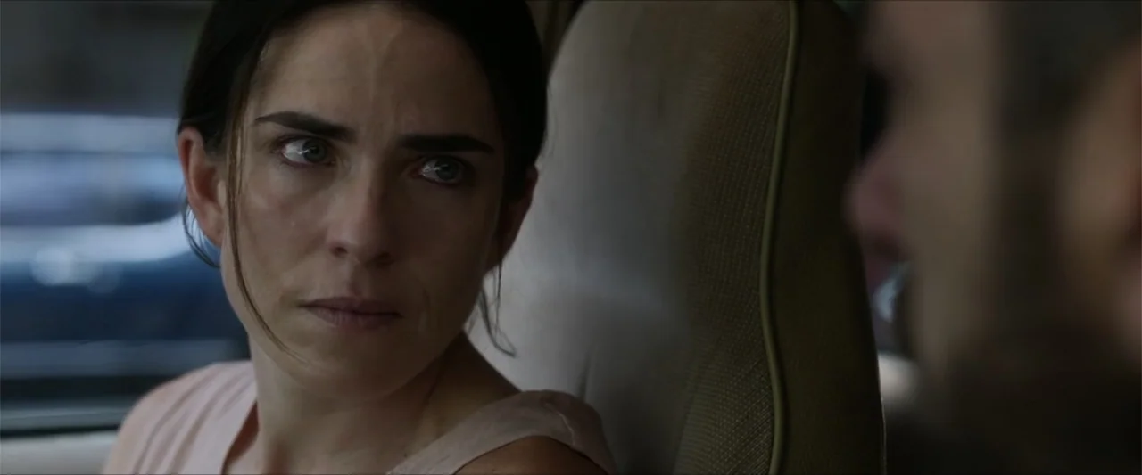 Dive (2013) movie still: closeup — The interior of a vehicle with a beige headrest visible behind the subject. A woman looks toward an unseen person…
