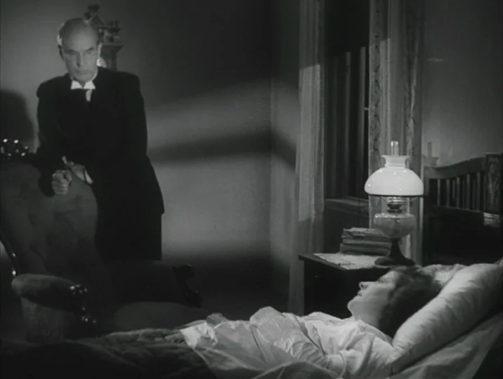 Crisis (1946) movie still: medium — A dimly lit room features a hospital bed with a woman lying down. An elderly man in a suit stands by a chair…