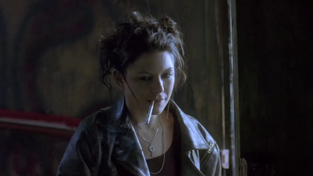 Hellraiser: Deader (2005) movie still: medium — A dimly lit interior room features dark walls and shadows behind the main subject. A woman with…