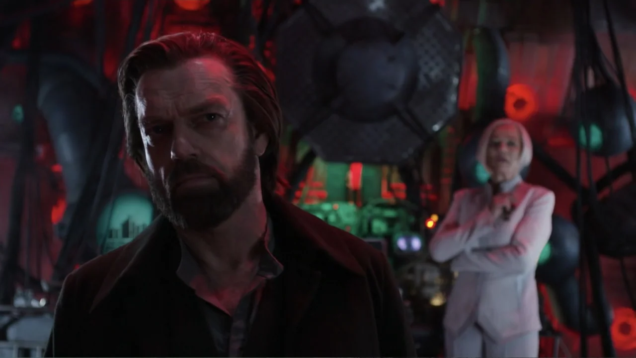 Mortal Engines (2018) movie still: medium — An industrial space filled with dark machinery cables and pulsating red light sources. A man with a…