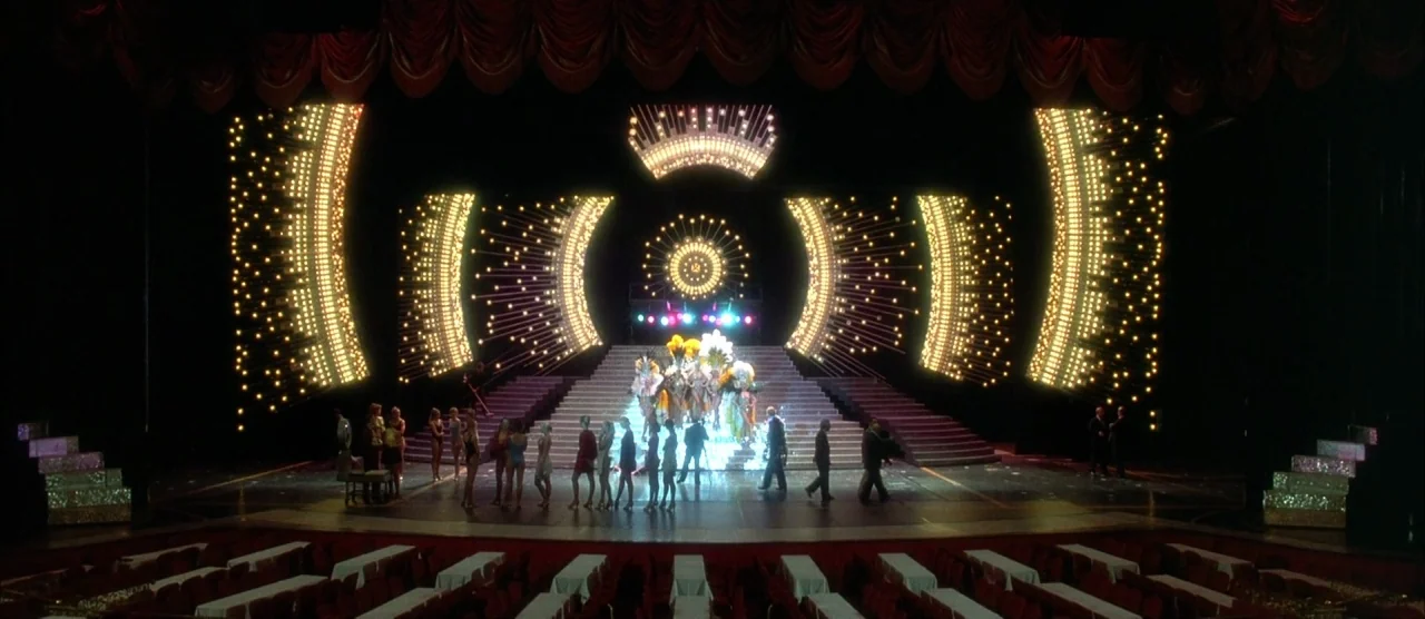 Casino (1995) movie still: wide — A wide shot shows a vast theatrical stage with ornate gold light patterns. A small group of performers and crew…