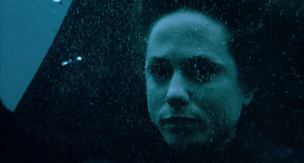 The Piano (1993) movie still: closeup — The face of a woman is visible just beneath the surface of dark water. Tiny air bubbles surround her…