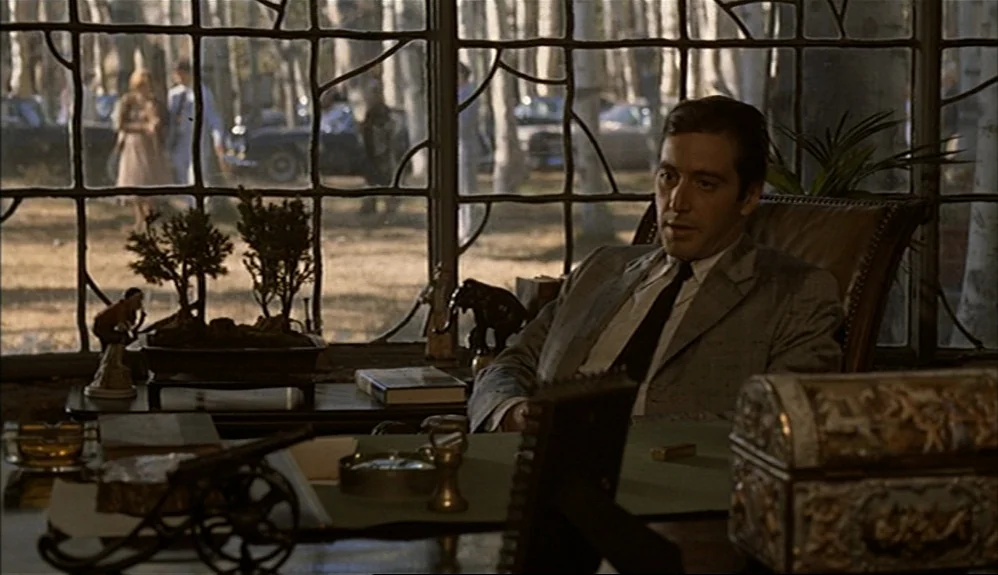 The Godfather Part II (1974) movie still: medium — A dark study features a large window with wrought-iron framing and outdoor trees visible. A man…