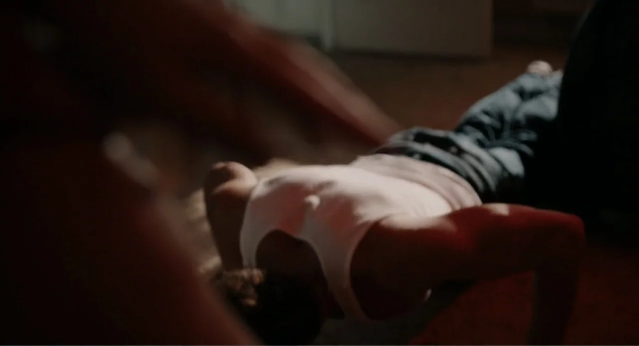 Ted Bundy: American Boogeyman (2021) movie still: medium — A dark, minimally furnished room contains a person exercising on a carpeted floor. A man…