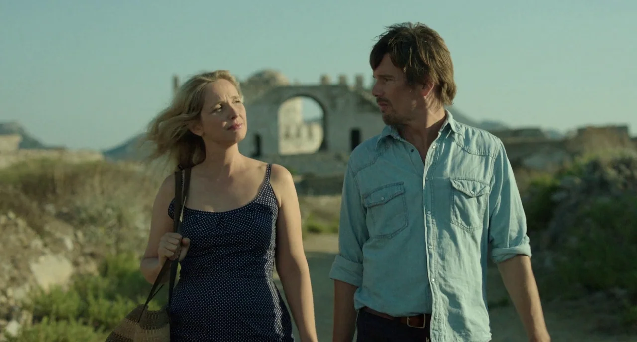 Before Midnight (2013) movie still: medium — A dry, open landscape features ancient stone archway ruins in the distance. A man and a woman walk…