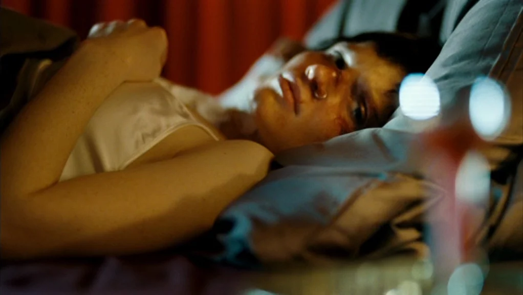 We Are The Night (2010) movie still: medium — A dark, dimly lit space contains a person resting in a bed. The subject lies under gray sheets while…