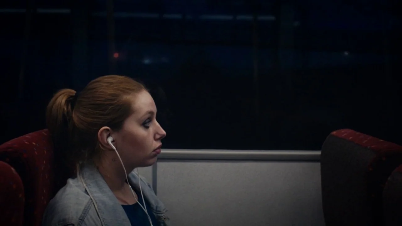 A Date for Mad Mary (2016) movie still: medium — A dark train car interior shows a window looking out into the night. A young woman sits in a…