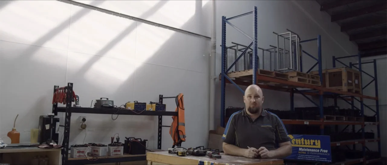 Bludgeon (2018) movie still: medium — A warehouse interior features tall metal shelving units filled with various batteries and crates. A man stands…