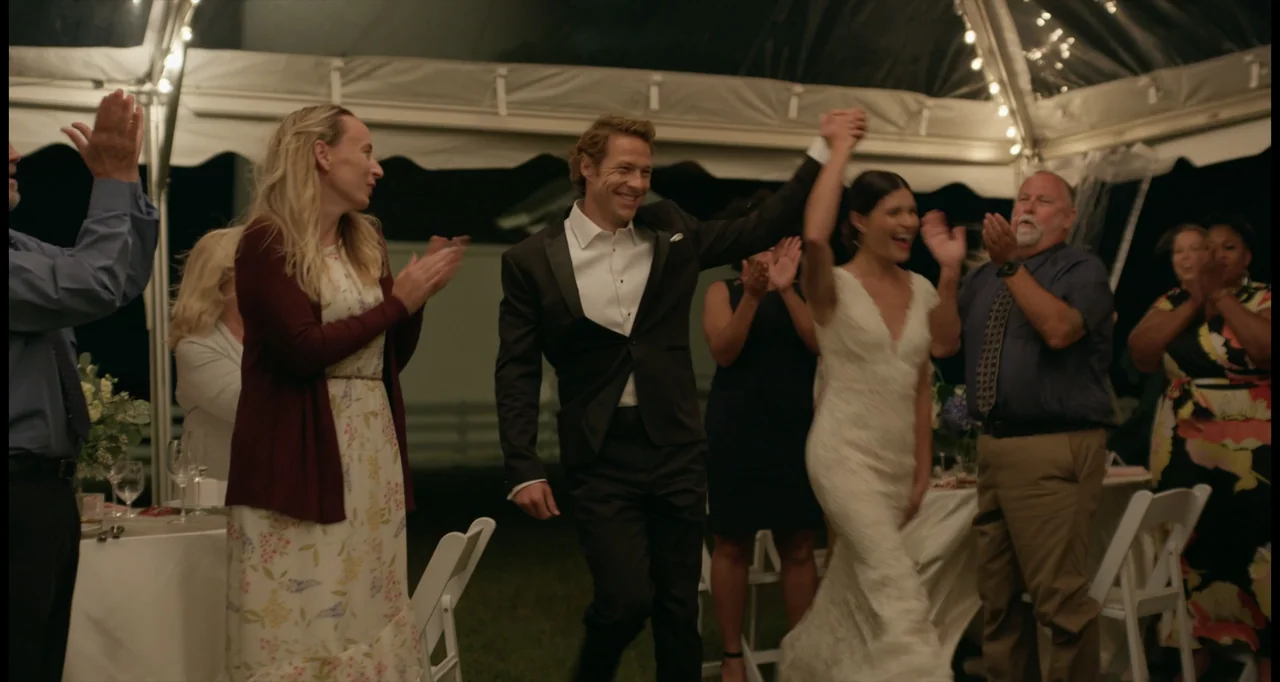 One True Loves (2023) movie still: fullbody — People at a nighttime outdoor wedding reception celebrate under a white canopy tent. A newlywed couple…