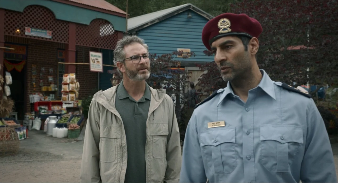 Ice Road: Vengeance (2025) movie still: medium — A man in a beige jacket and a uniformed officer stand before a shop. The officer looks toward the…