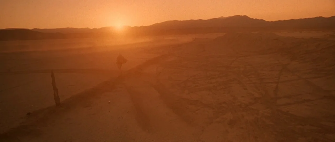 Fear and Loathing In Las Vegas (1998) movie still: wide — A vast, empty desert landscape stretches toward low, hazy mountains during sunset. Tire…