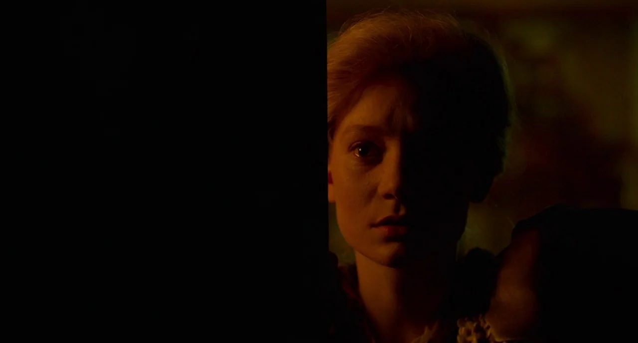 Crimson Peak (2015) movie still: closeup — A woman's face emerges from the darkness in a dimly lit, undefined indoor space. She looks directly ahead…