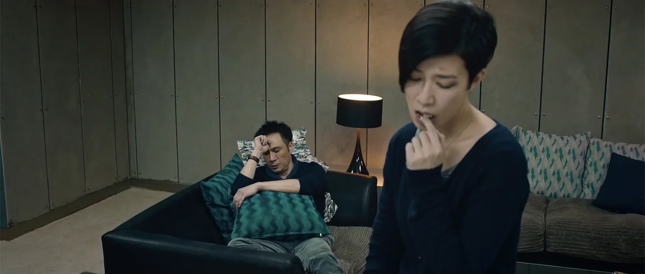 Line Walker (2016) movie still: medium — A modern lounge with grey paneled walls and dark seating features a lamp. A woman examines her teeth while…