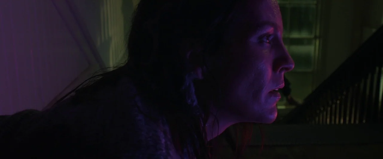 Before I Wake (2016) movie still: closeup — A dark indoor space features a wooden staircase railing in the background. A woman stares off-camera…