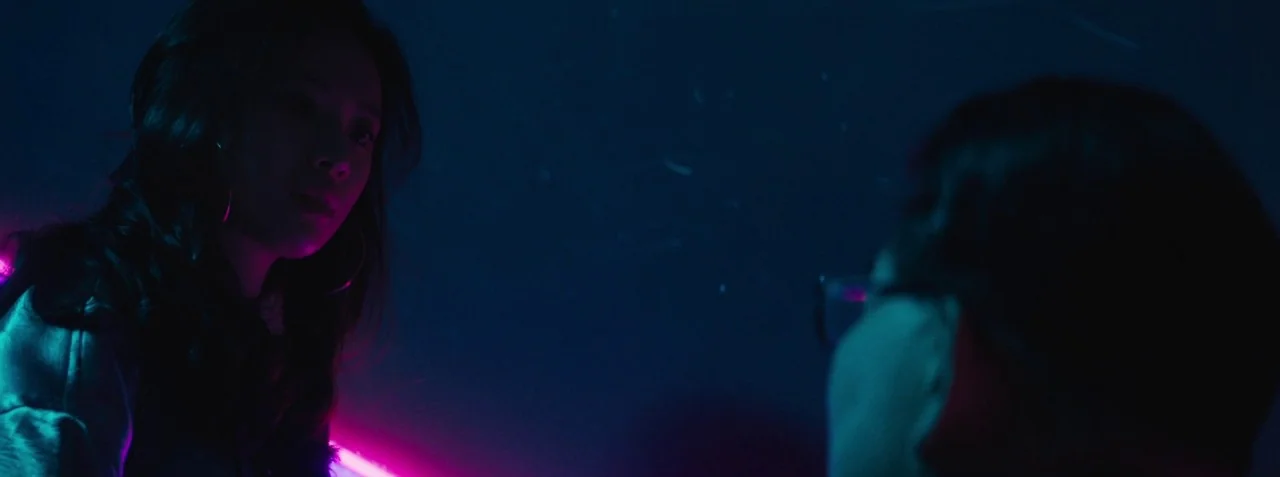 Dead Pigs (2018) movie still: medium — A dark, neon-lit space with high-contrast magenta and blue ambient lighting. A woman looks toward a person…