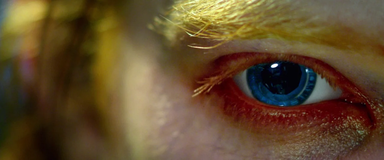 Dredd (2012) movie still: closeup — An extreme close-up focuses on a single human eye with a vibrant blue iris. Fine details of the eyelash line and…