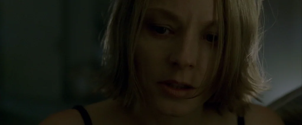 Panic Room (2002) movie still: closeup — A dimly lit room with muted, cool-toned decor visible in the shadows. A blonde woman in a black tank top…