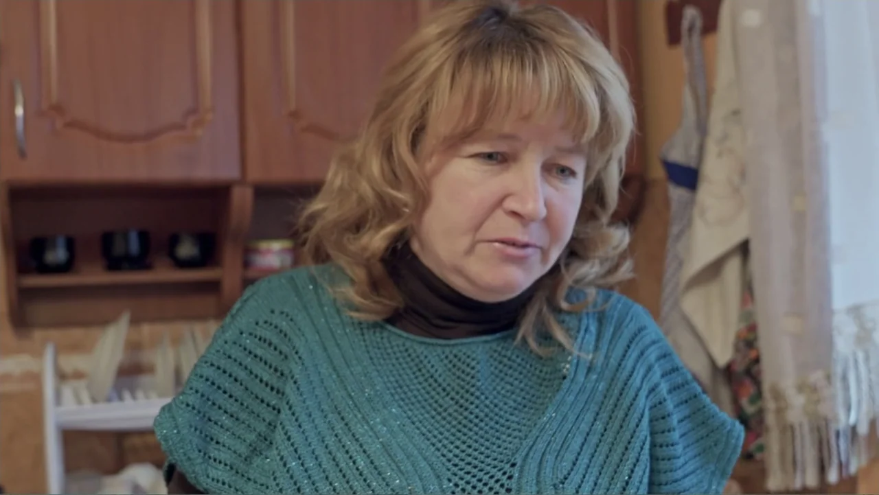 Finding the Way Home (1991) movie still: medium — A domestic interior with wooden cabinets, a drying rack, and hanging kitchen towels. A middle-aged…