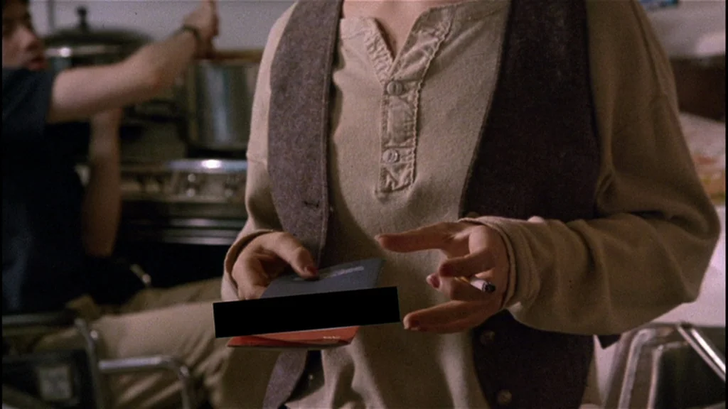 Goodfellas (1990) movie still: medium — A cluttered kitchen with a person in a vest holding a book and cigarette. Another person is visible in the…