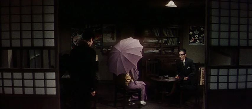 Jigoku (1960) movie still: wide — A dimly lit room features traditional Japanese sliding doors framing the main space. Two men converse with a…