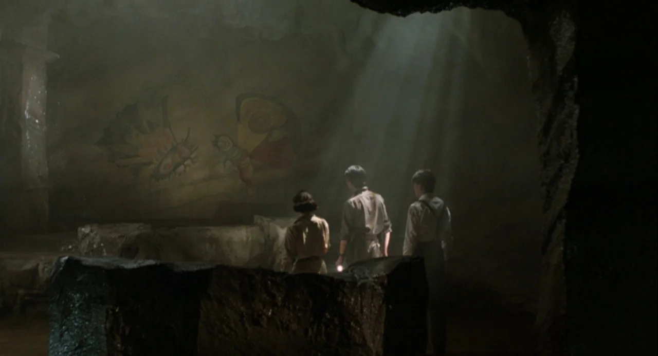 Godzilla and Mothra: The Battle for Earth (1992) movie still: wide — A dark subterranean cavern features a large prehistoric mural painted on the…