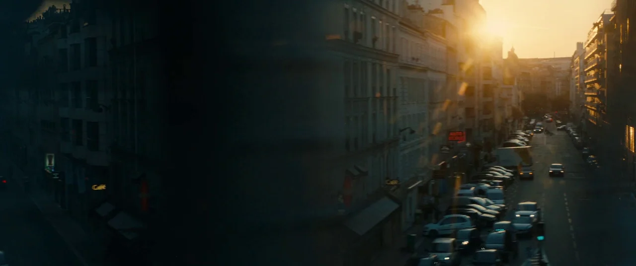 BPM (Beats Per Minute) (2017) movie still: establishing — A dense urban street in Paris is framed by multistory buildings on both sides. Cars travel…
