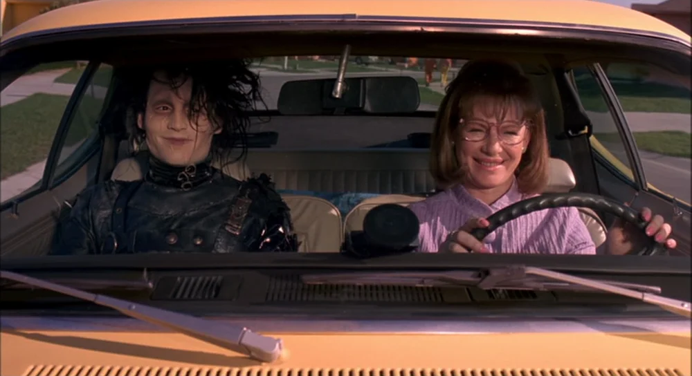 Edward Scissorhands (1990) movie still: medium — A bright yellow car interior with a man and woman in the front seats. The two figures look ahead…