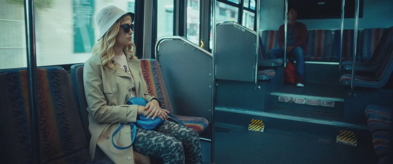 Gemini (2017) movie still: medium — A quiet bus interior features patterned seats and a metal divider between seating sections. A woman sits in the…