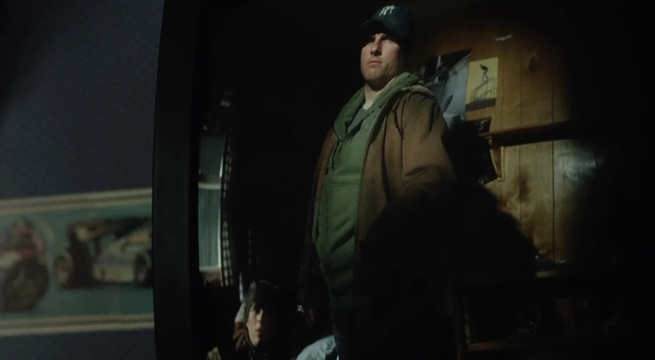 War of the Worlds (2005) movie still: medium — A dark bedroom with wood paneling walls adorned with small posters and decals. A man stands in the…