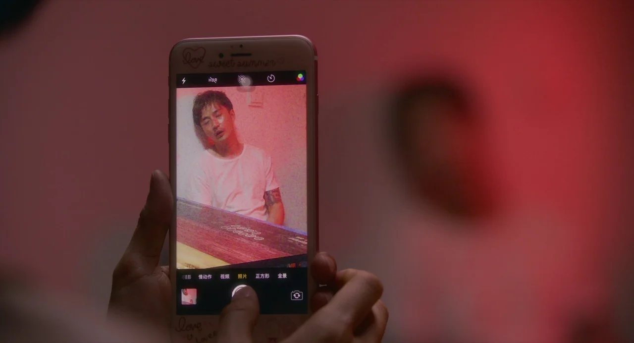 White River (2023) movie still: closeup — A close view of a smartphone screen displaying a photo of a man. The phone is held by unseen hands against…