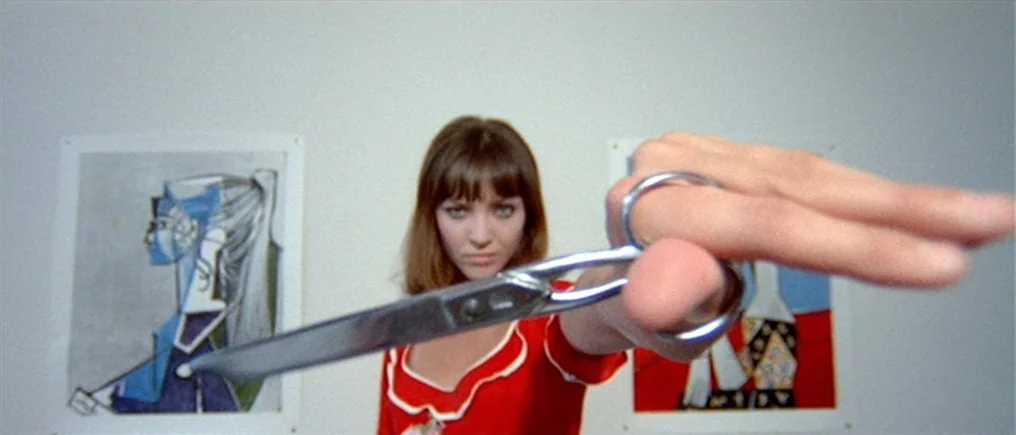 Pierrot Le Fou (Crazy Pete) (1965) movie still: medium — A woman stands before a white wall displaying two framed abstract paintings. She extends…