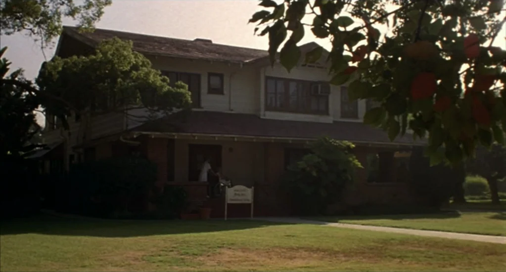 Bubba Ho-Tep (2002) movie still: establishing — A two-story residential-style building with a covered porch stands behind a manicured green lawn. A…