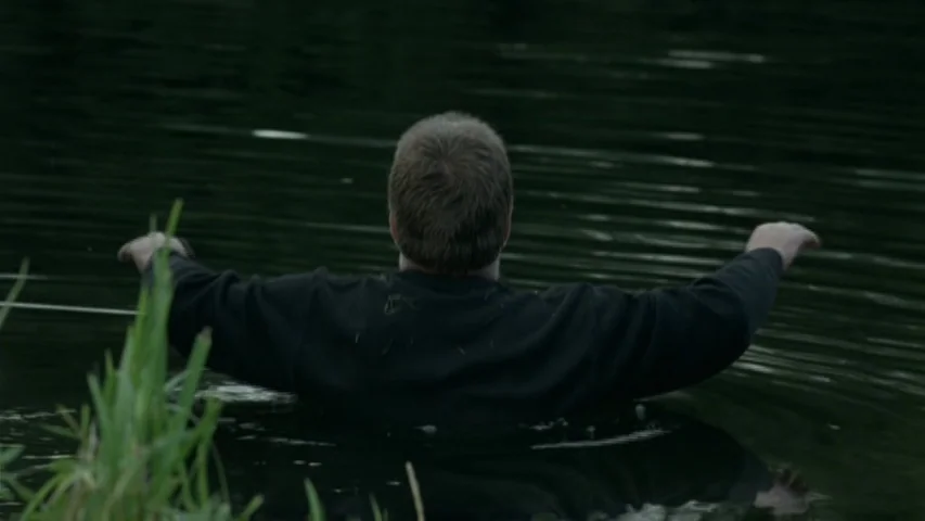 Garage (2007) movie still: medium — A man stands chest-deep in a dark, murky body of water surrounded by reeds. He faces away from the camera with…