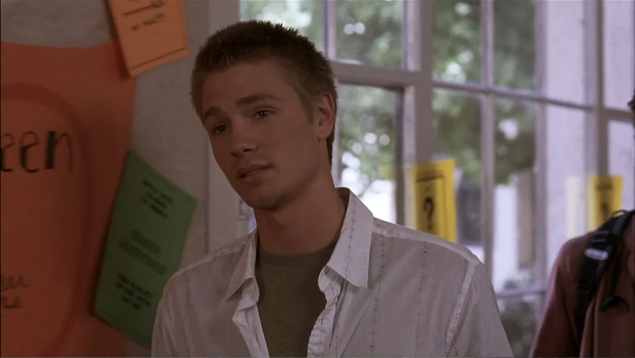A Cinderella Story (2004) movie still: medium — A high school hallway with paper notices taped to a light-colored wall. A young man stands in front…
