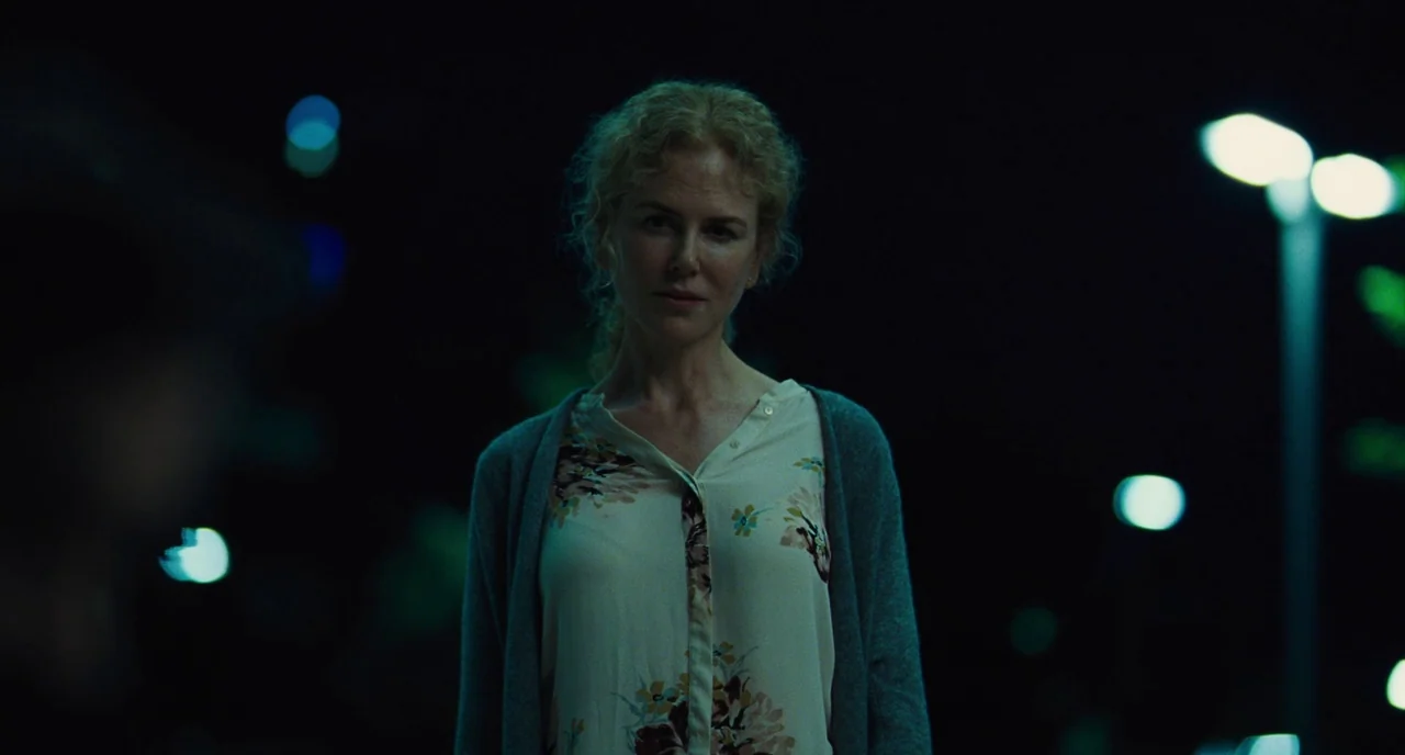 The Killing of a Sacred Deer (2017) movie still: medium — A woman stands in a dark parking lot at night with blurred lights behind her. She faces…