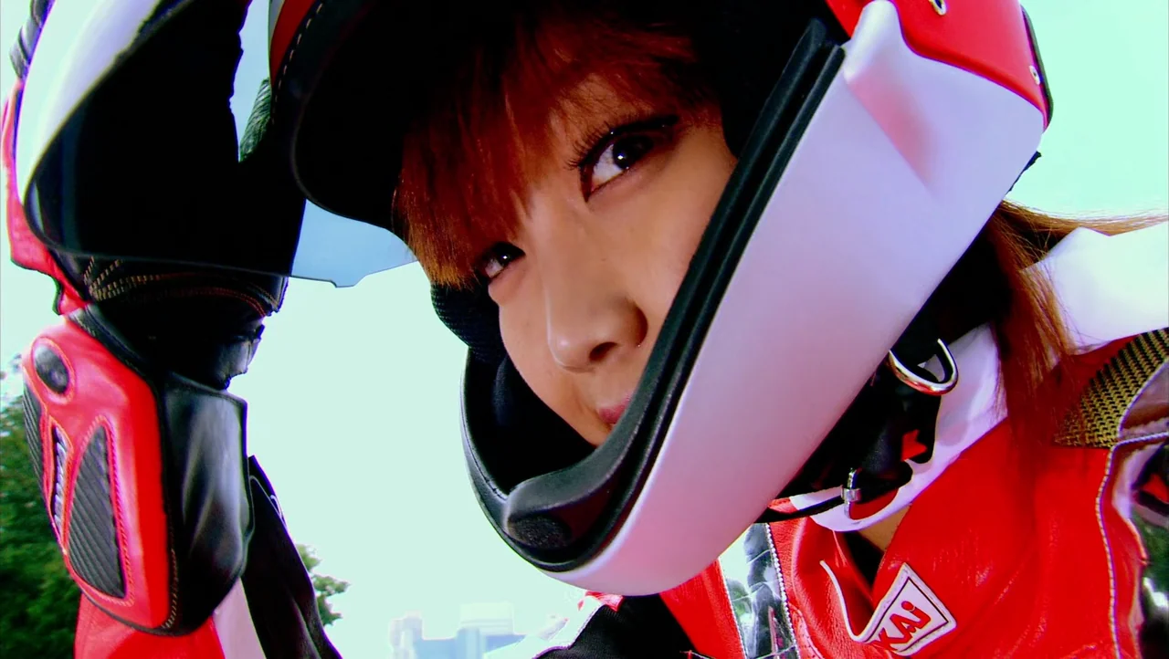 Cutie Honey (2004) movie still: closeup — A person wears a red and white racing helmet while standing outdoors. They look down into the camera lens…