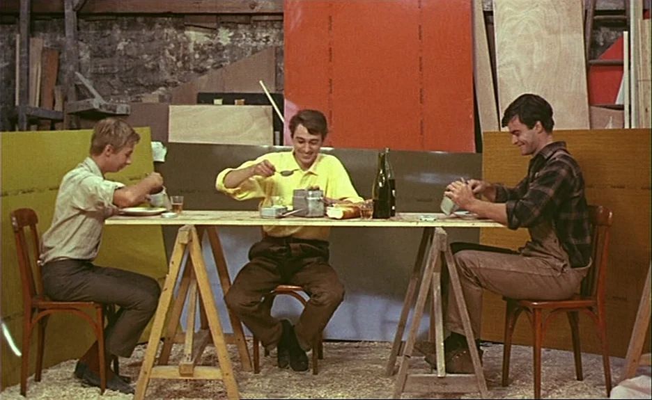 Le Bonheur (Happiness) (1965) movie still: wide — An interior workshop features stone walls covered by colorful plywood boards and wooden sawhorses.…