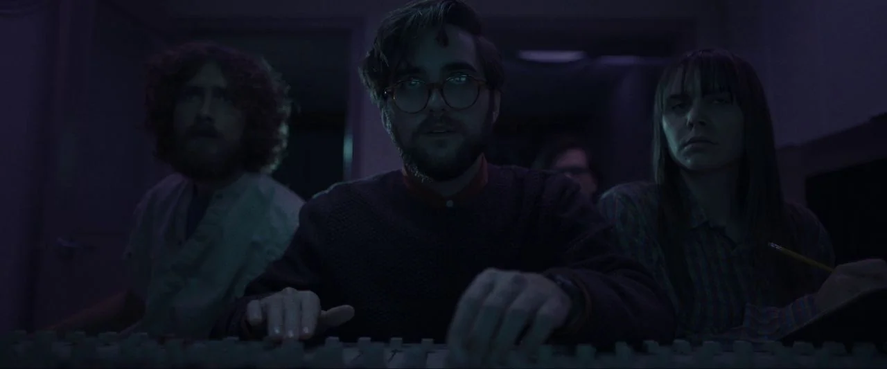 Come True (2020) movie still: medium — A dimly lit recording studio environment is filled with complex audio mixing hardware. Three people sit…