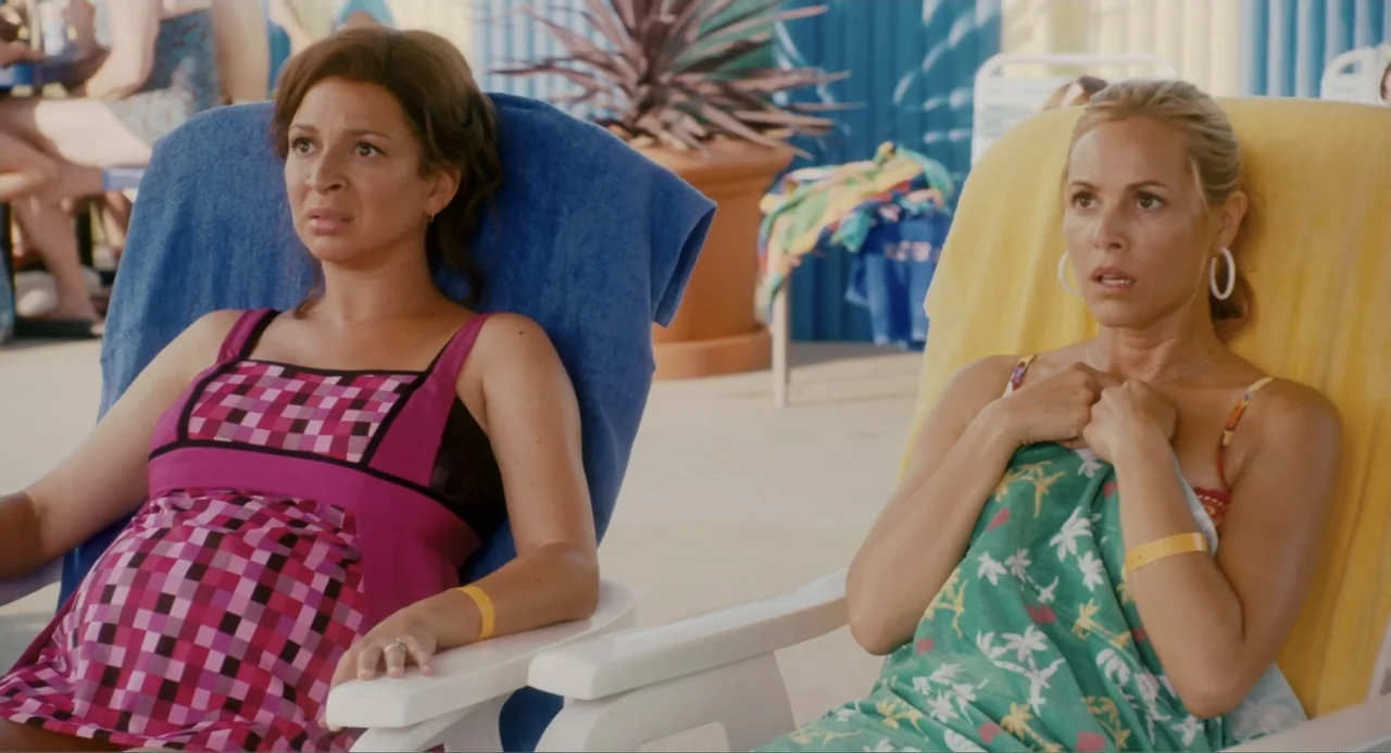 Grown Ups (2010) movie still: medium — A bright outdoor pool deck with blue and yellow lounge chairs. Two women sit in chairs looking forward with…