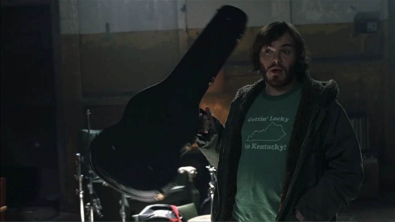 School of Rock (2003) movie still: medium — An interior space with industrial features and muted wall tones. A bearded man stands holding a…