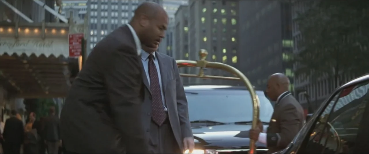 Maid in Manhattan (2002) movie still: medium — A city hotel entrance at dusk with a car parked by the curb. A man in a suit steps out of a vehicle…