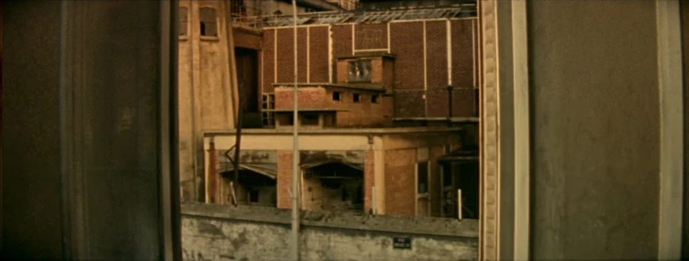 I Stand Alone (Seul Contre Tous) (1998) movie still: establishing — An exterior view of brick industrial buildings is framed by vertical window…