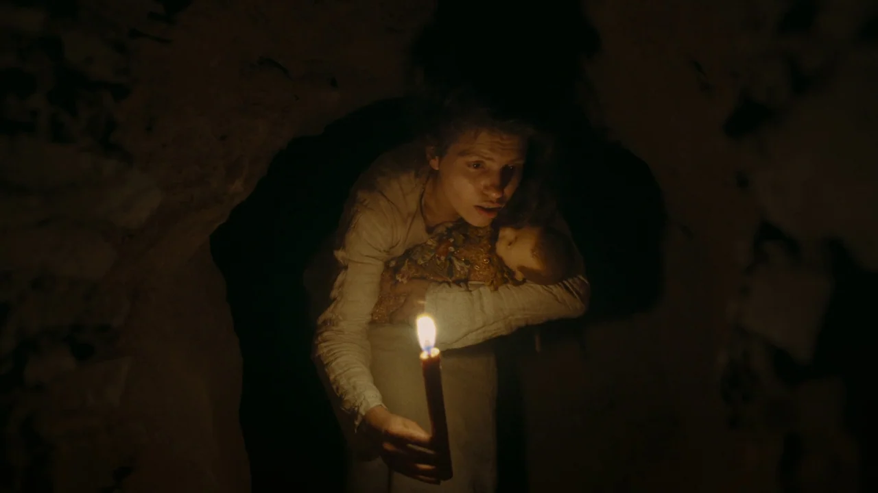 The Devil’s Bath (2024) movie still: medium — A dark, cramped stone cave interior with rough-hewn walls surrounds the subjects. A young woman…