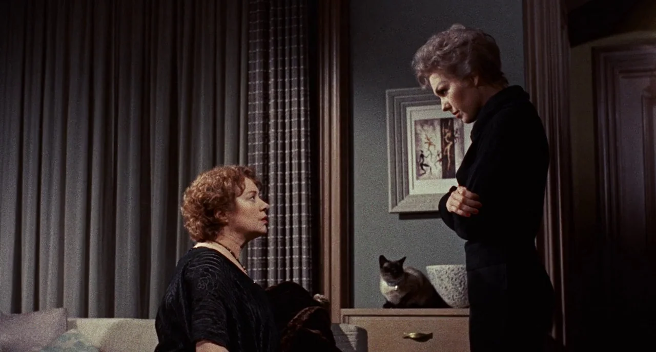 Bell Book and Candle (1958) movie still: medium — A 1950s living room features heavy floor-to-ceiling curtains and a framed wall painting. One woman…