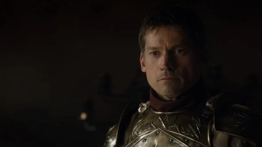Game of Thrones (2015) movie still: closeup — A dark stone interior features a man in gold armor illuminated by faint light. The subject is looking…